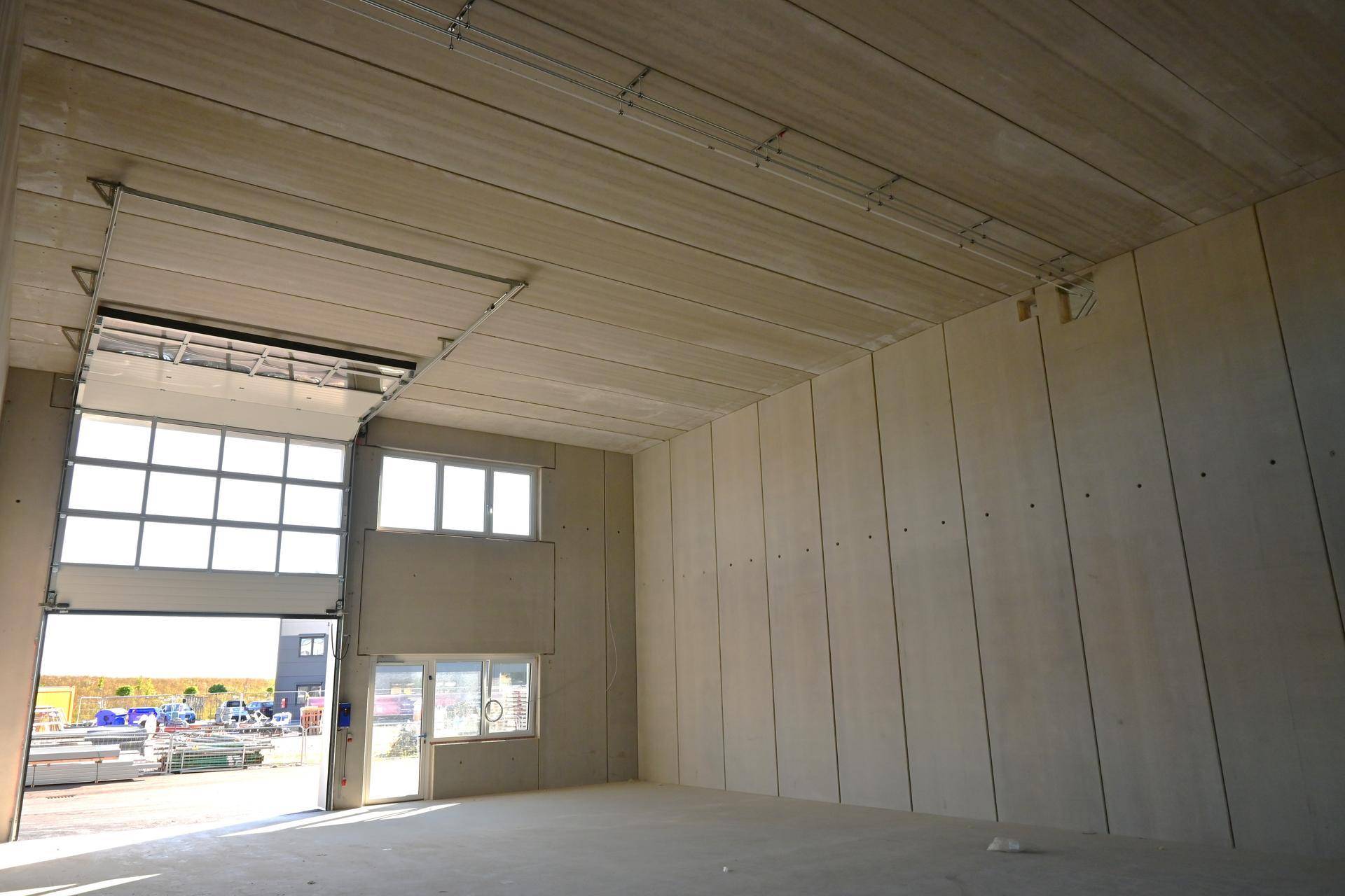 Geräumige, leere Lagerhalle mit hohen Decken, Betonwänden und einem großen Eingangstor.