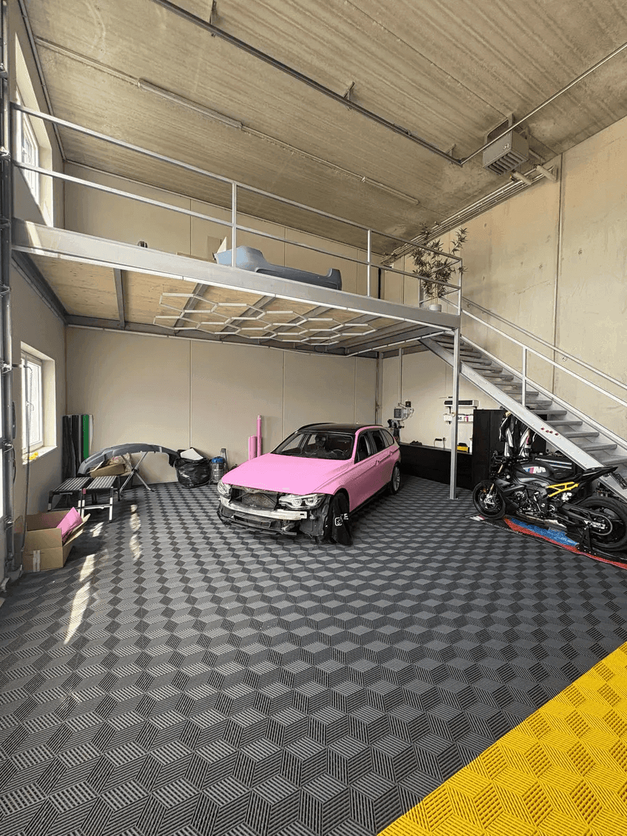 Geräumige Werkstatt mit hoher Decke, Betonwänden, einer Mezzanine-Ebene und einem gemusterten Fliesenboden.