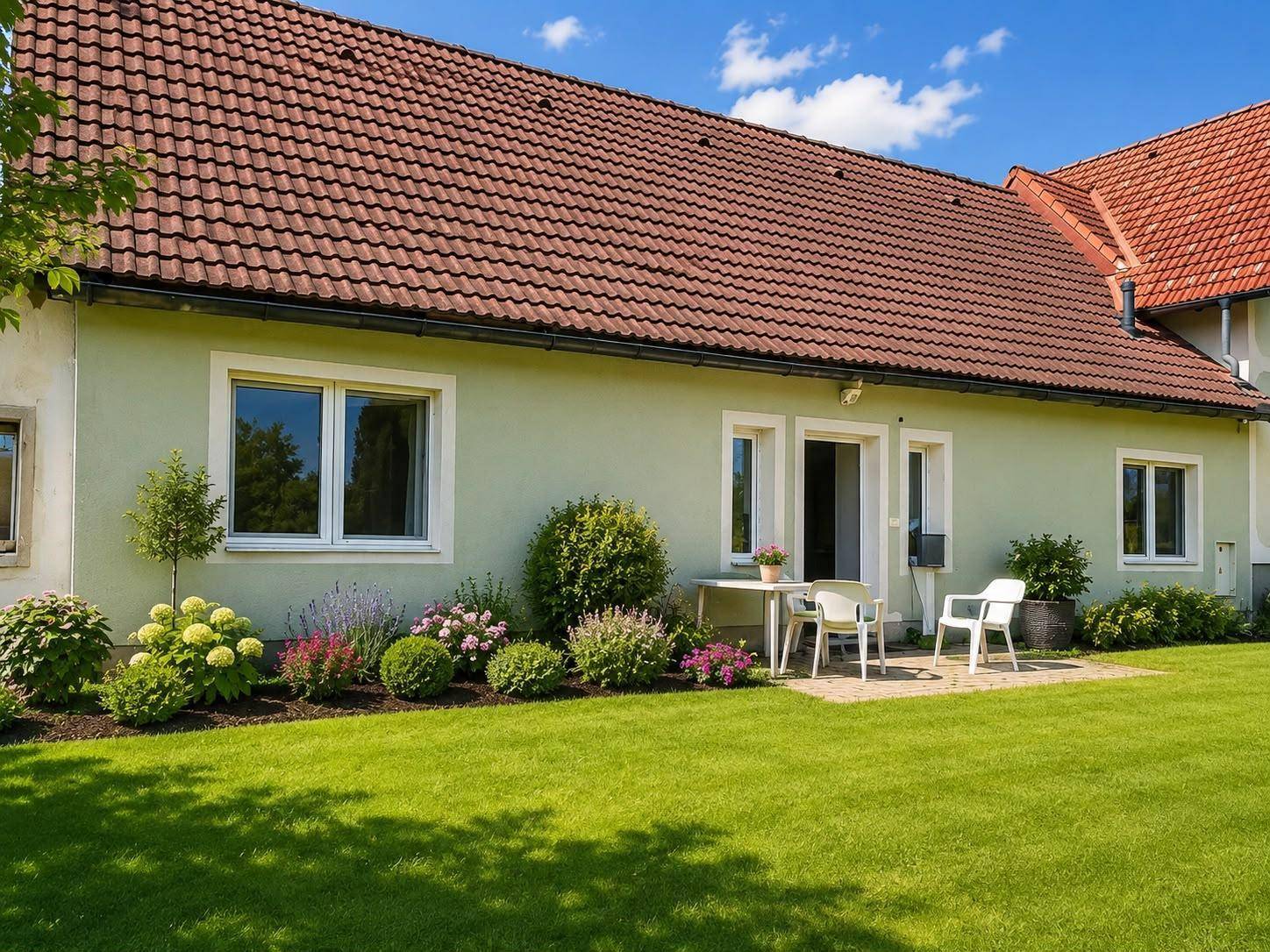 Rückseite des Hauses mit kleiner Terrasse, Gartenmöbeln und weitläufiger Rasenfläche.