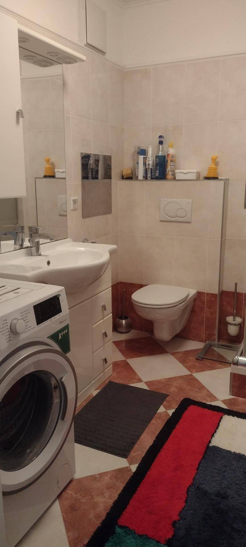 Badezimmer mit Waschbecken, Toilette und Waschmaschine, ausgestattet mit hellen und roten Fliesen.