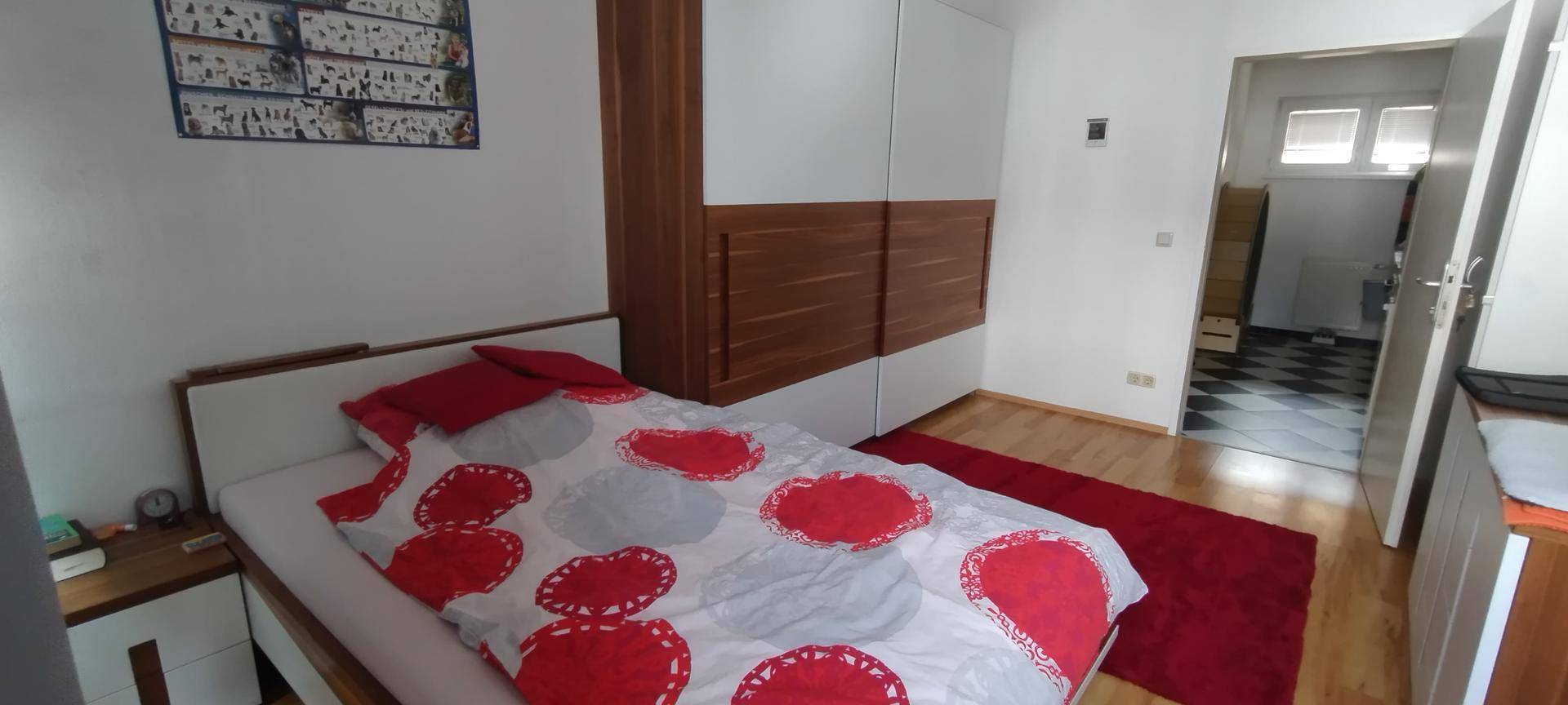 Gemütliches Schlafzimmer mit einem Bett, einem großen Kleiderschrank und einem roten Teppich.