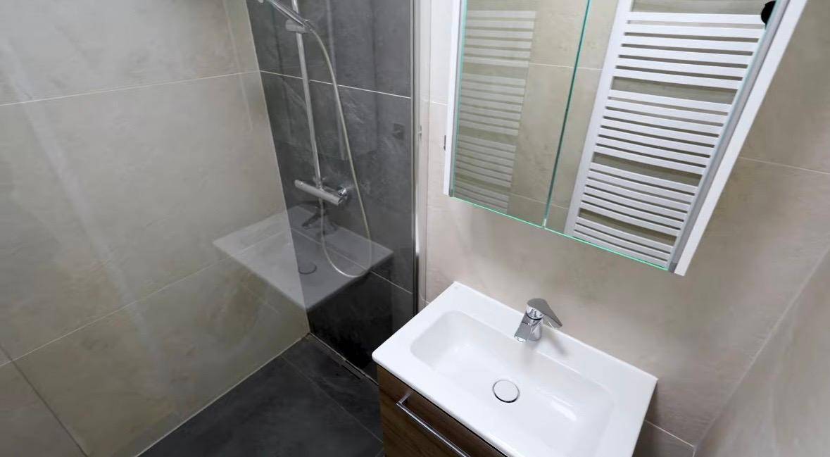 Modernes Badezimmer mit ebenerdiger Dusche, Waschbecken, Spiegelschrank und beheiztem Handtuchhalter.