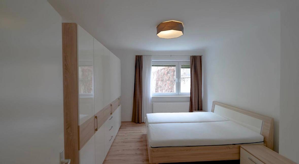 Helles Schlafzimmer mit Doppelbett, großem Kleiderschrank und Fenster für natürliche Belichtung.