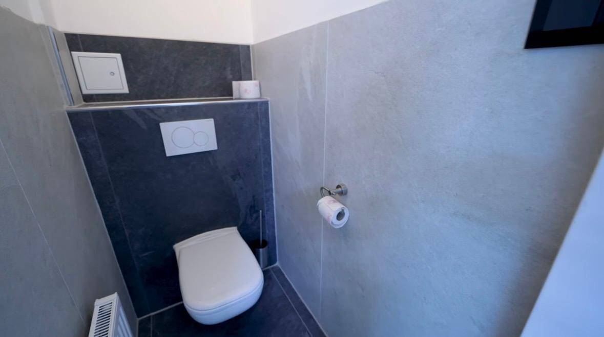 Separates WC mit wandhängender Toilette und modernen grauen Fliesen, funktional und sauber.