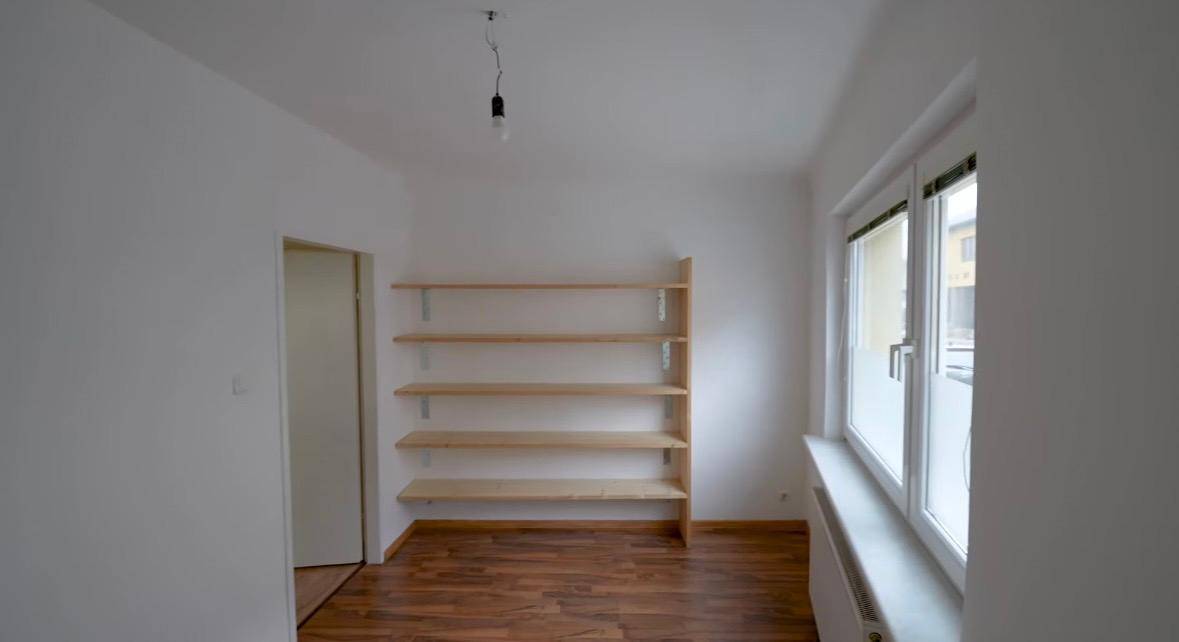 Helles Zimmer mit Holzböden und praktischen Wandregalen, ideal als Büro oder Gästezimmer nutzbar.