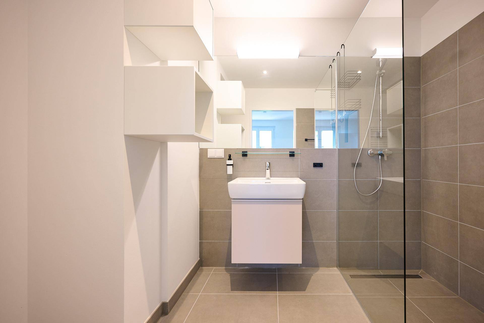 Modernes Badezimmer mit Waschbecken, großem Spiegel und begehbarer Dusche.