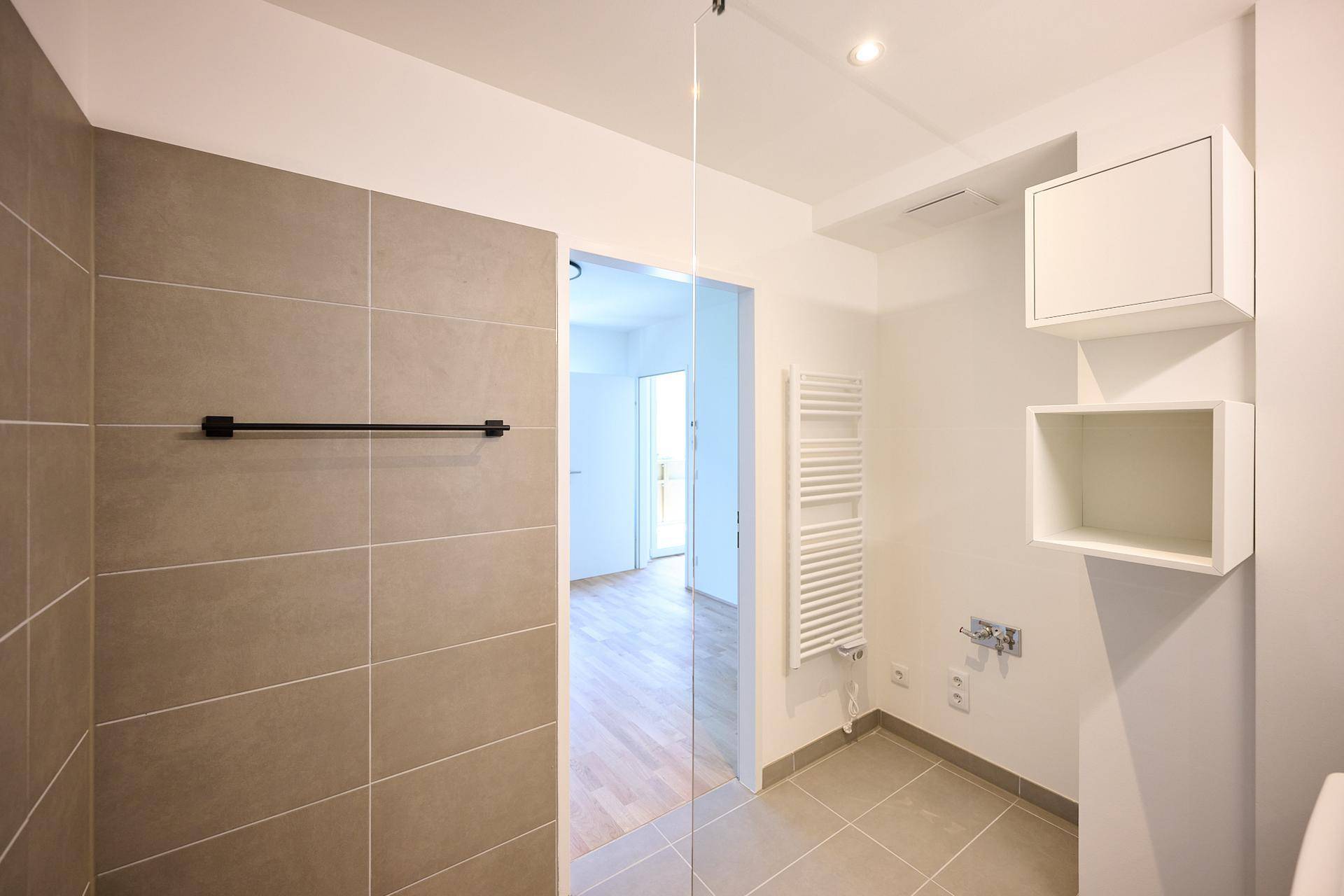 Modernes Badezimmer mit begehbarer Dusche, grauen Fliesen und Handtuchheizkörper.