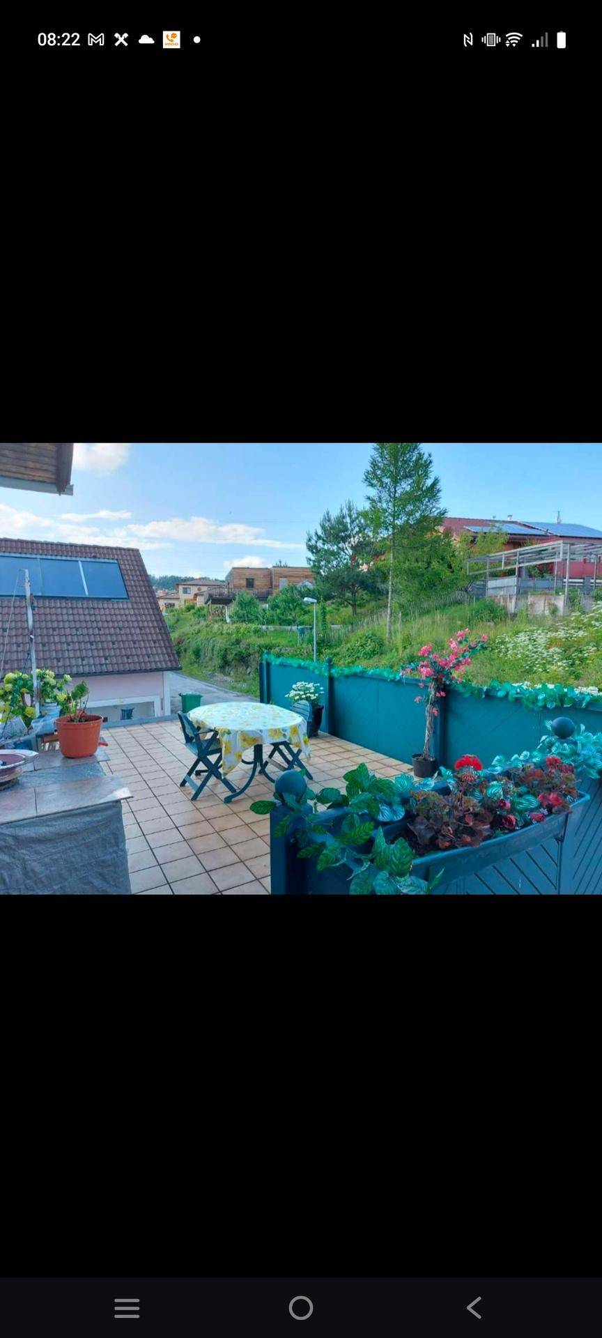 Gemütliche Fliesenterrasse mit Esstisch, Stühlen und bunten Blumenkästen, mit Blick auf die Umgebung.