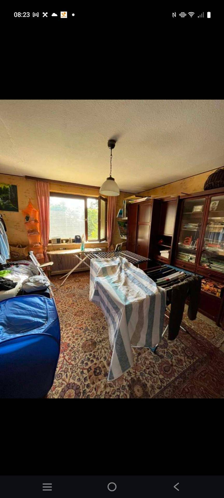 Vielseitiger Raum mit Teppichboden, Fenster und verschiedenen Möbeln, inklusive Wäscheständer.