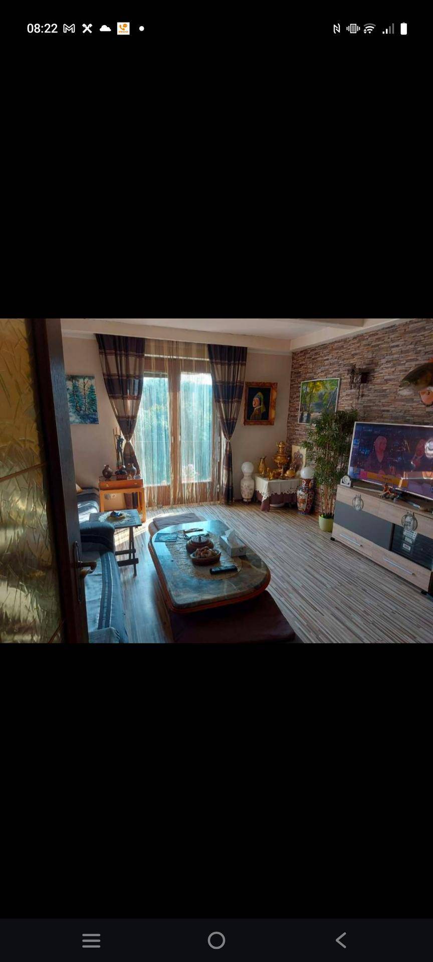 Gemütliches Wohnzimmer mit Holzboden, großer Fensterfront und einer Wand in Ziegeloptik.
