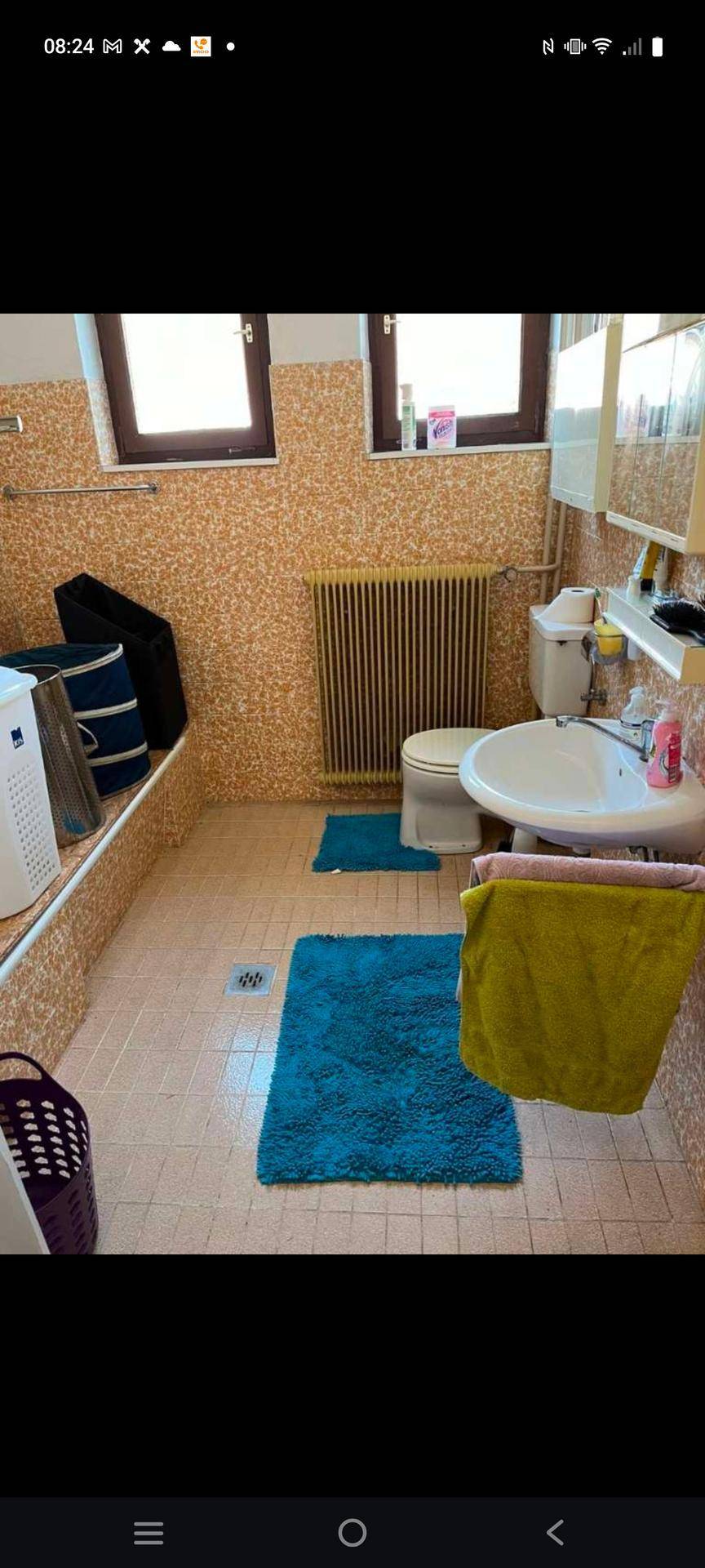 Badezimmer mit beigefarbenen Fliesen an Wänden und Boden, ausgestattet mit Toilette, Waschbecken und Heizkörper.