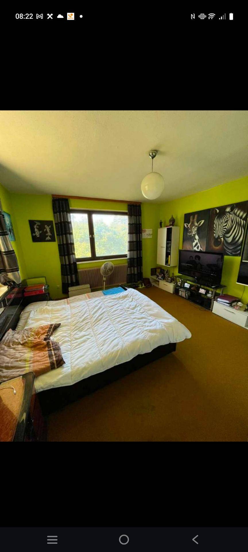 Schlafzimmer mit Bett, leuchtend grünen Wänden und einem Fenster für natürliches Licht.