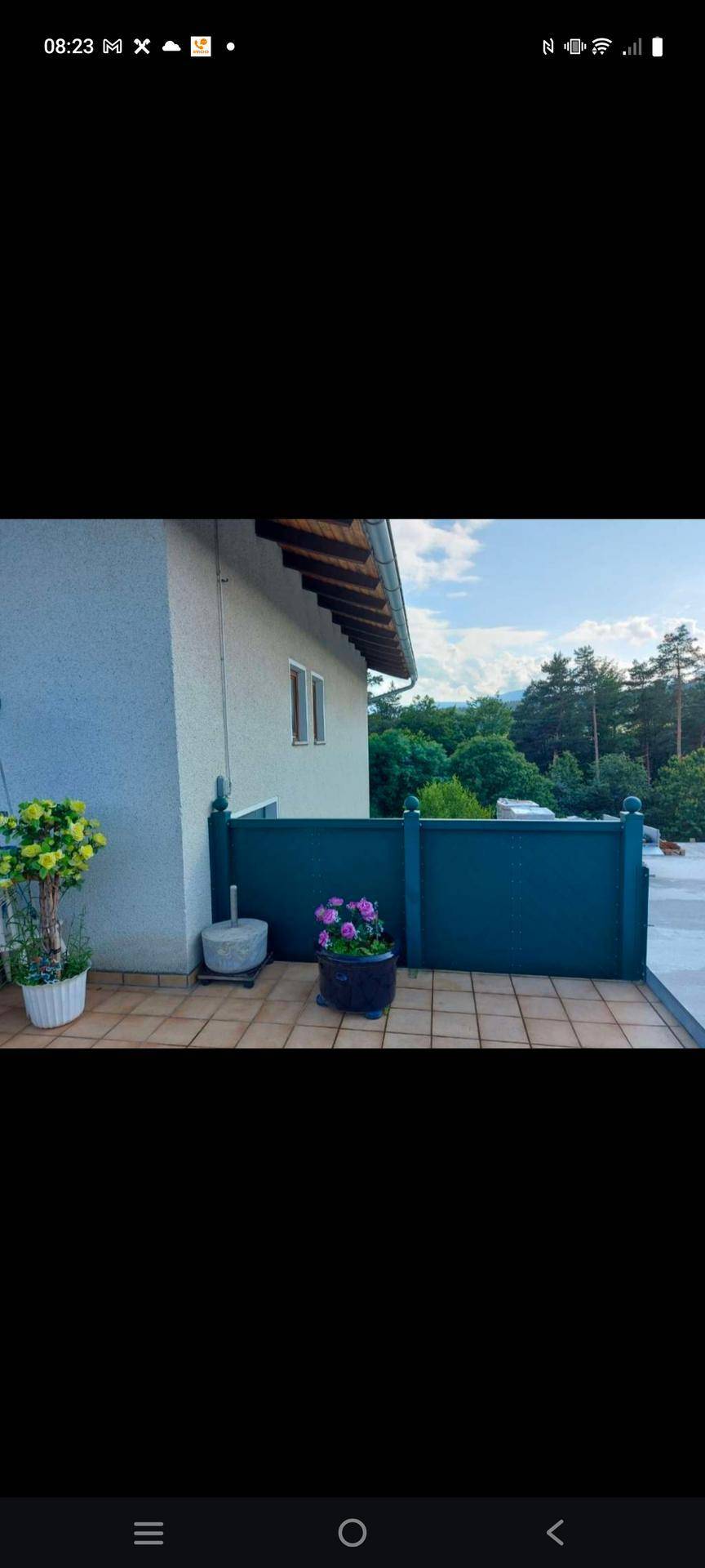 Teil einer gefliesten Terrasse mit Topfpflanzen und einem weiten Blick ins Grüne.