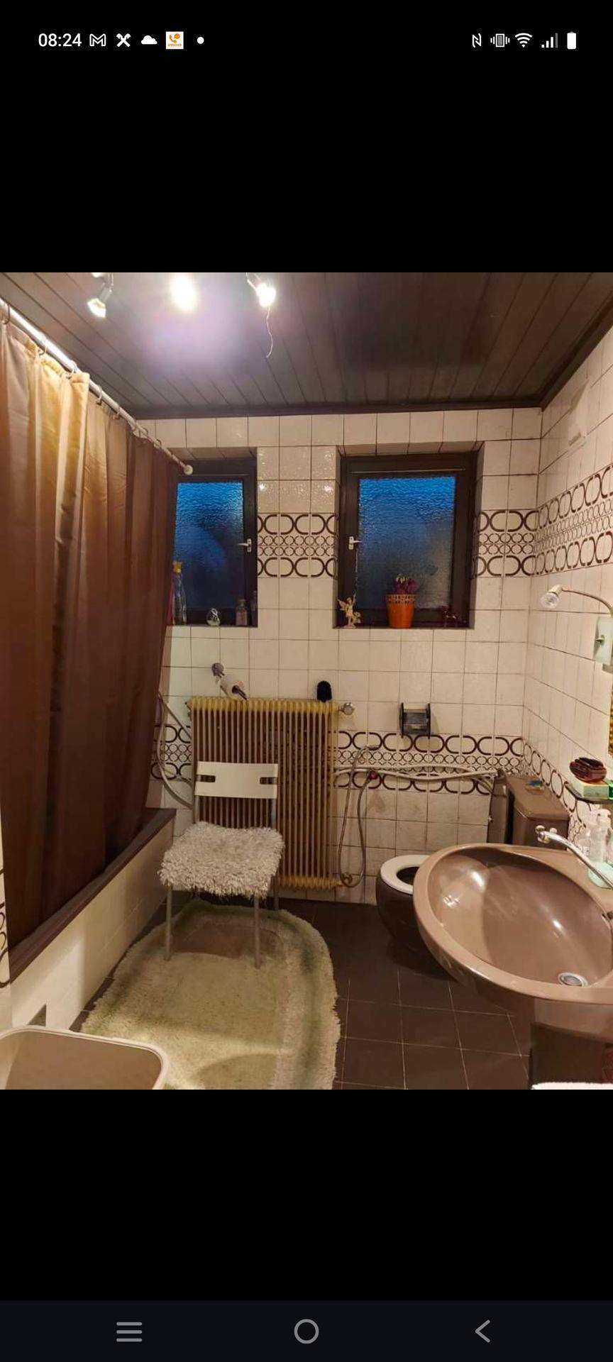 Badezimmer mit Duschvorhang, gemusterten Fliesen, Waschbecken und Toilette, mit Fenster.