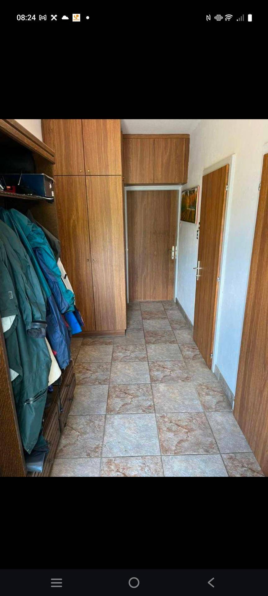 Flur mit Einbauschränken aus Holz und gefliestem Boden, der zu weiteren Räumen führt.