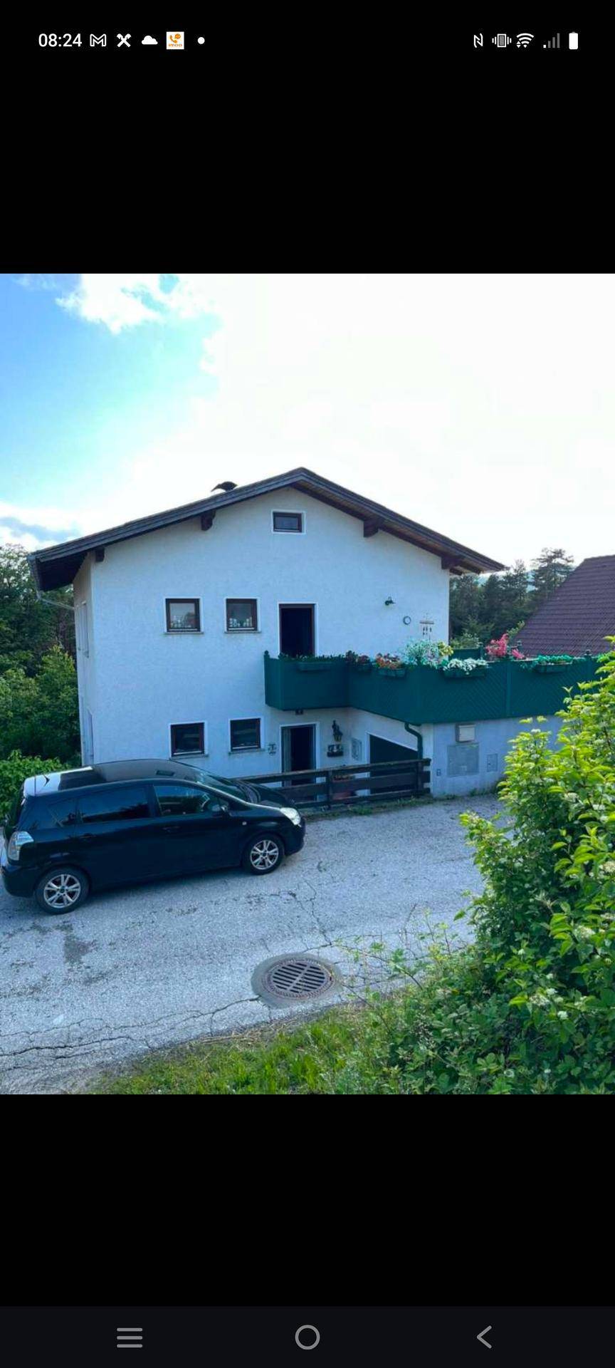 Vorderansicht des Hauses mit Eingangsbereich, Balkon und einem geparkten Auto auf der Auffahrt.