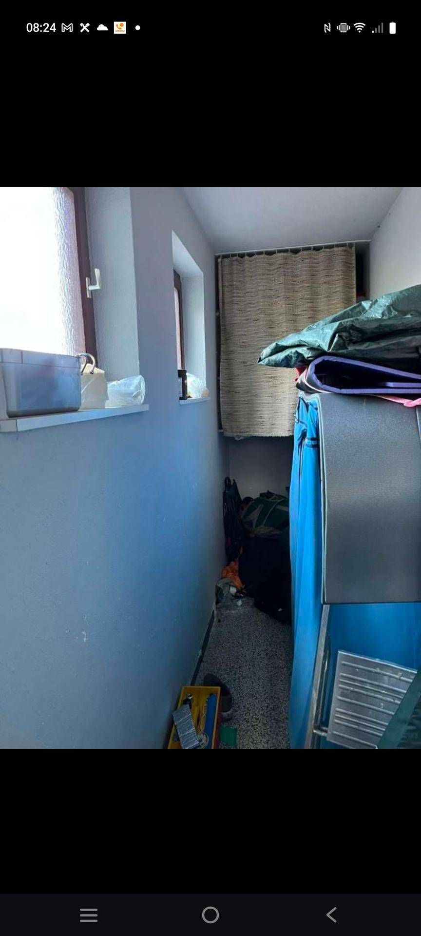 Schmaler Innenraum mit einem Fenster und verschiedenen gelagerten Gegenständen, möglicherweise ein Abstellraum.