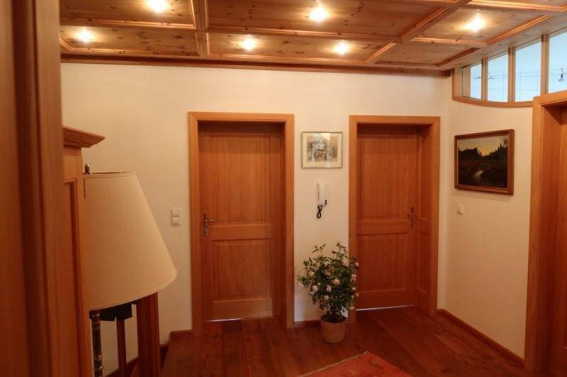 Heller Flur mit zwei Holztüren, Holzboden und einer Decke mit Holzpaneelen.