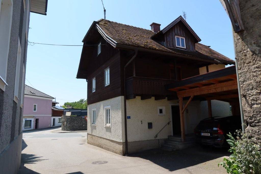 Seitenansicht des Hauses mit Carport und traditioneller Holzverkleidung unter blauem Himmel.