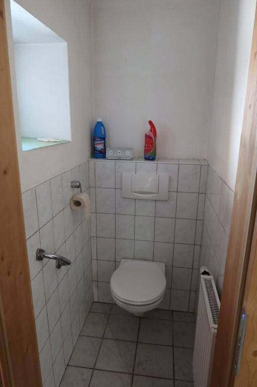 Separate Toilette mit Wand-WC und Fliesen an den Wänden und auf dem Boden.