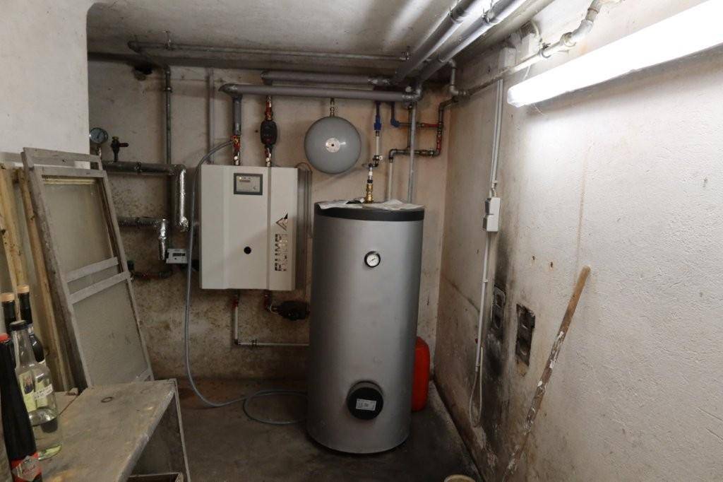 Heizungsraum mit Warmwasserspeicher und sichtbaren Rohrleitungen.