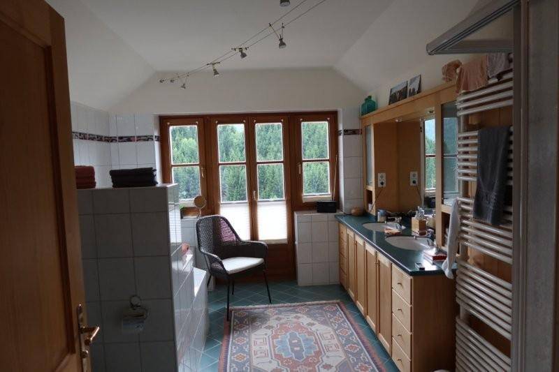 Geräumiges Badezimmer mit Doppelwaschbecken, Badewanne und großem Fenster mit Waldblick.