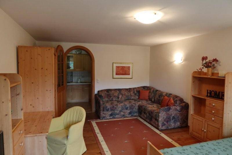 Wohnzimmer mit Ecksofa, Holzmöbeln und einem Durchgang zu einer kleinen Kochnische.
