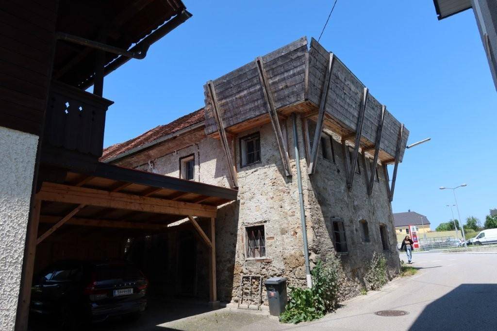 Altes Steingebäude mit Holzanbau und Carport, das historische Bausubstanz zeigt.