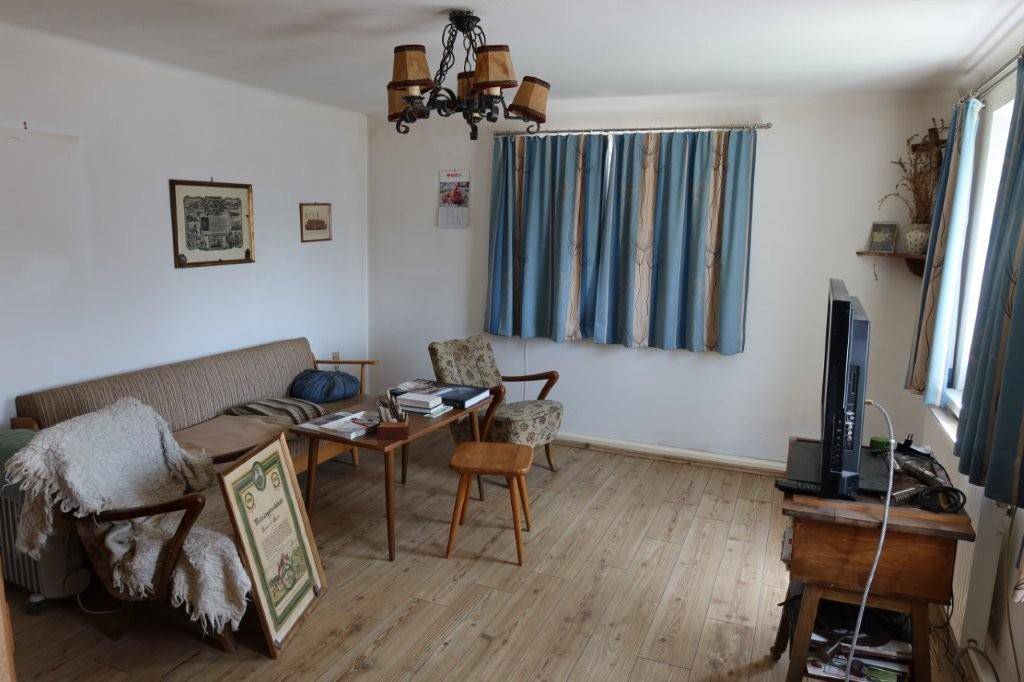 Wohnzimmer mit traditionellen Möbeln, Holzboden und Fenstern mit Vorhängen.
