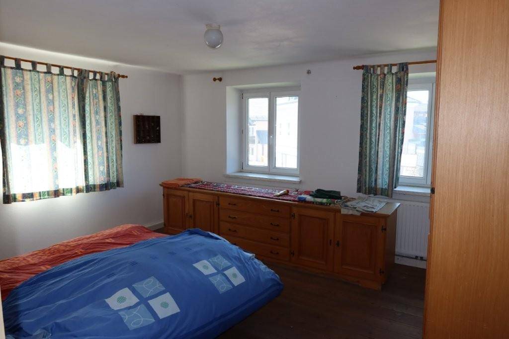 Schlafzimmer mit Holzboden, großem Schrank und zwei Fenstern für viel Licht.