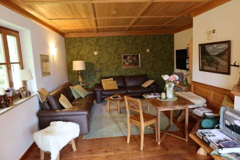 Rustikales Wohnzimmer mit Ledersofas, gemusterter Tapete und einer Holzkassettendecke.