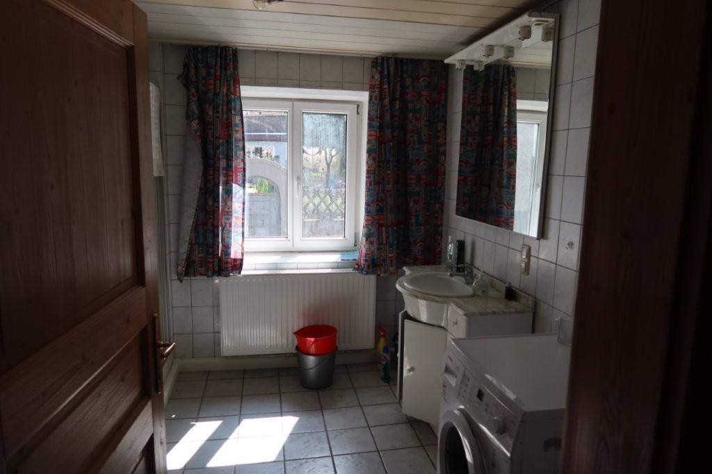 Badezimmer mit Fliesenboden, Waschmaschine und Fenster für Tageslicht.