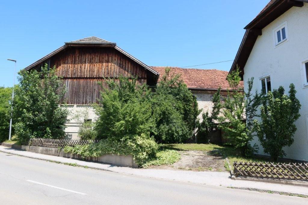 Ansicht des alten Nebengebäudes mit Holzwänden und Ziegeldach, umgeben von Bäumen.