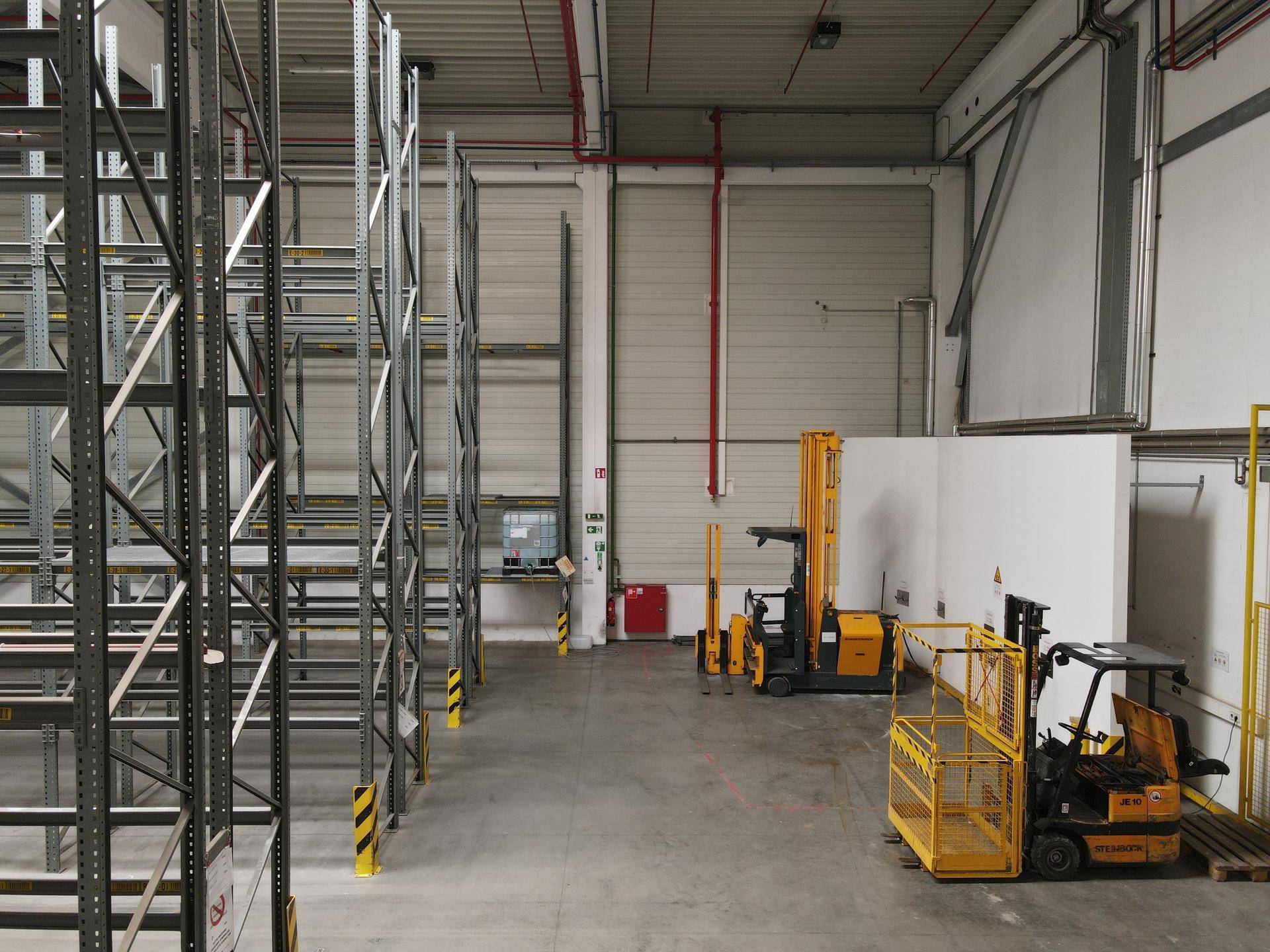 Geräumige Lagerhalle mit leeren Regalen, Betonboden und zwei gelben Gabelstaplern, bereit für den Betrieb.
