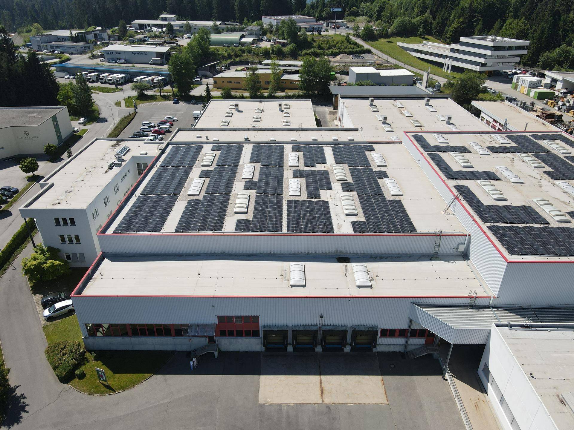 Luftaufnahme des Hauptgebäudes eines Industriekomplexes mit einer großen Photovoltaikanlage auf dem Dach.
