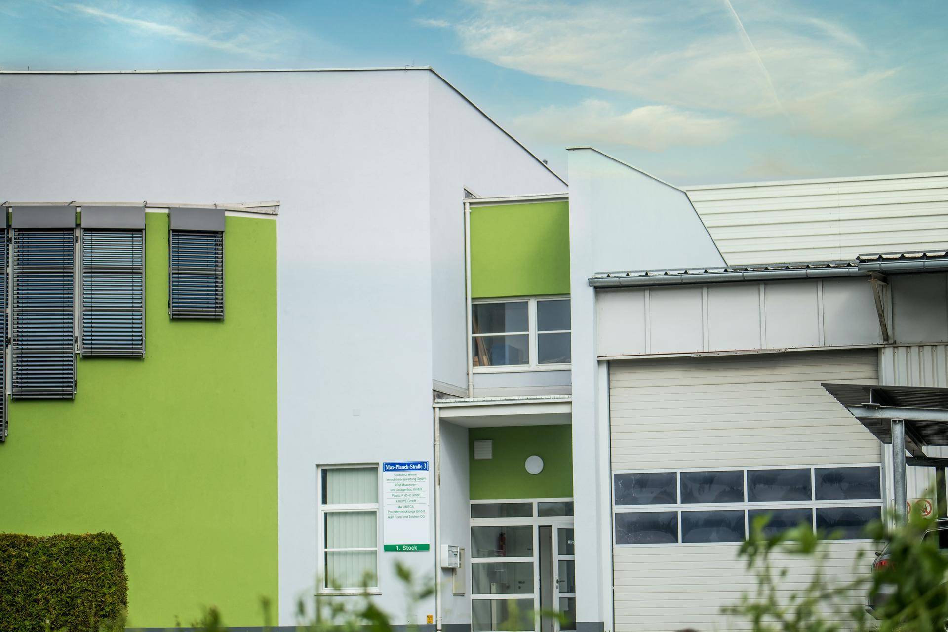 Detailansicht der modernen Gebäudefassade mit grünen Akzenten und Eingangsbereich unter blauem Himmel.