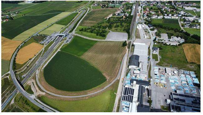 Luftaufnahme eines Industriegebiets mit Autobahnanschluss, umgeben von landwirtschaftlichen Flächen und Wohngebieten.