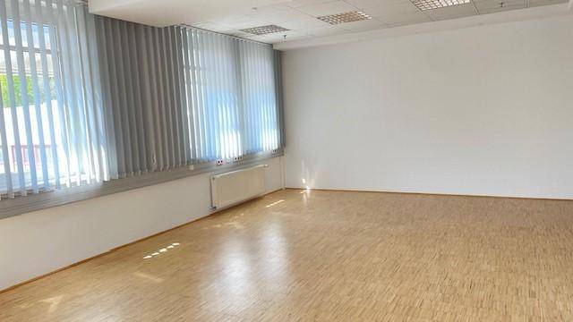 Geräumiger Büroraum mit hellem Holzfußboden und großen Fenstern, die viel Tageslicht hereinlassen.