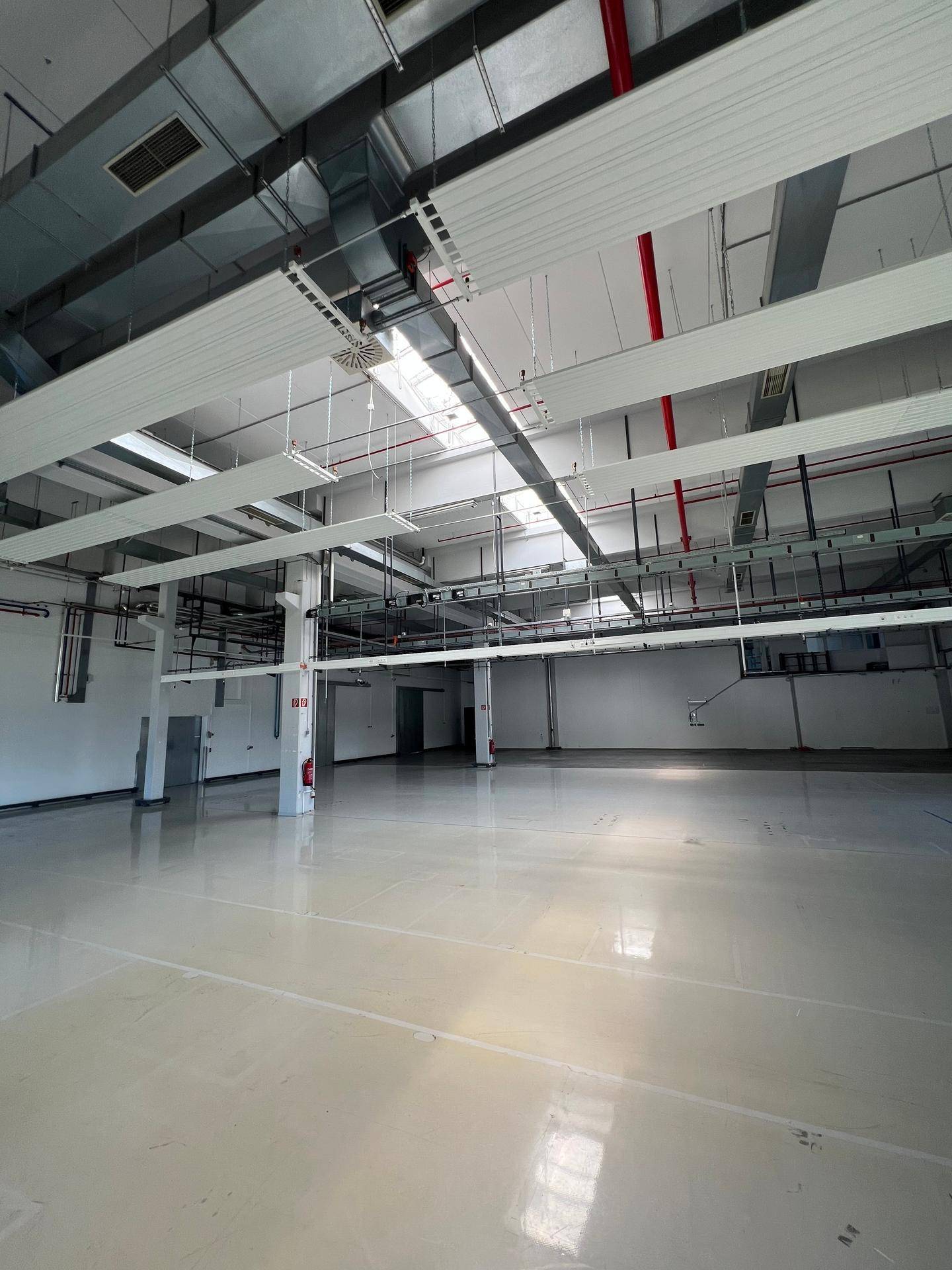 Weitläufige Industriehalle mit hohen Decken, glänzendem Boden und moderner Beleuchtung von oben.