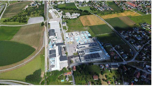 Luftaufnahme eines Industriegebiets mit Photovoltaikanlagen auf den Dächern, umgeben von Feldern und Wohnsiedlungen.