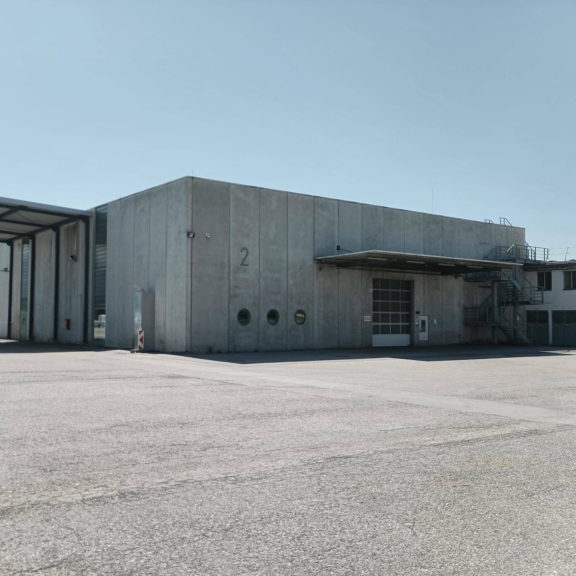 Industriegebäude mit Betonfassade, großem Rolltor und Außentreppe unter klarem Himmel.