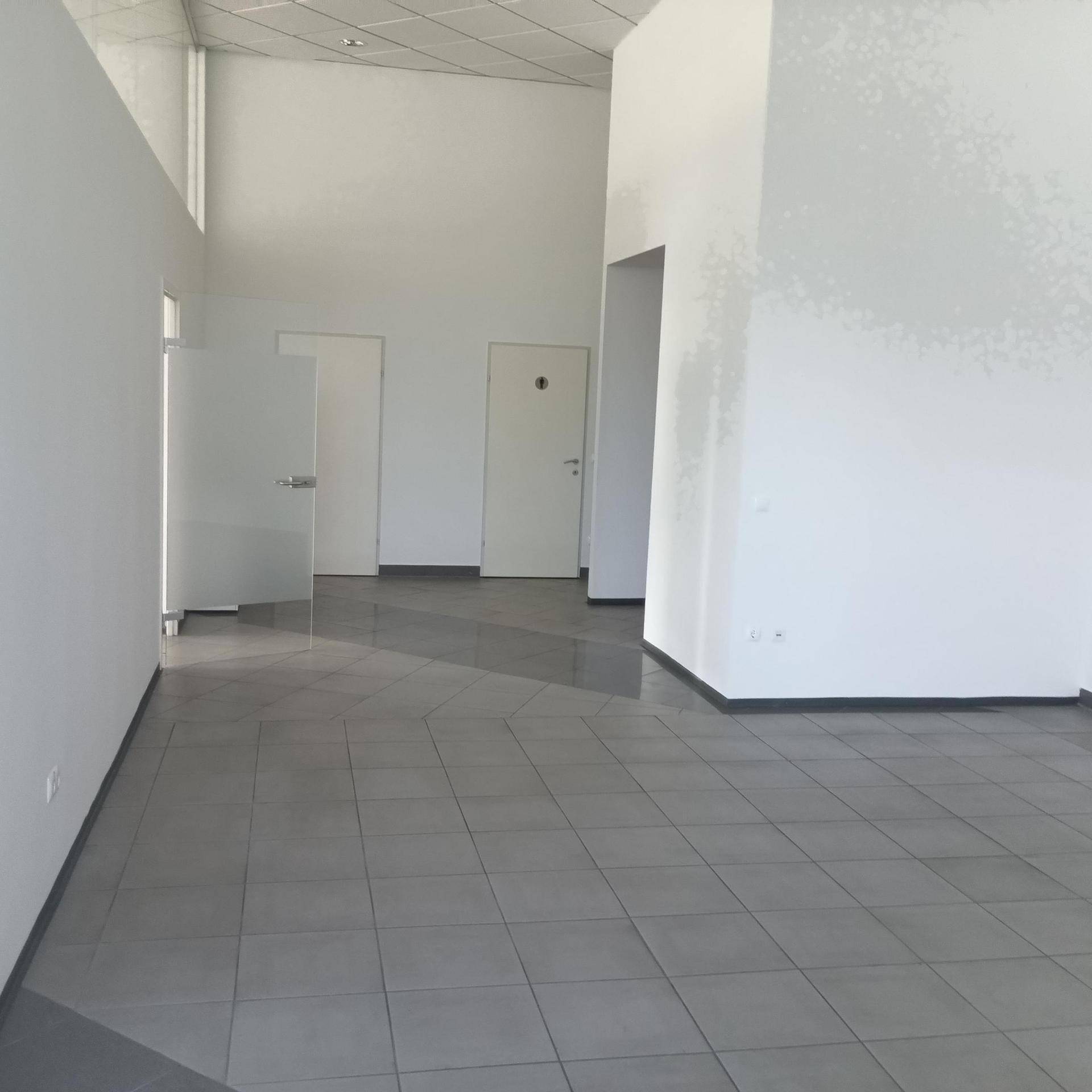 Großer, leerer Büroraum mit hohen Decken, Fliesenboden und mehreren Türen, der vielseitige Nutzungsmöglichkeiten bietet.