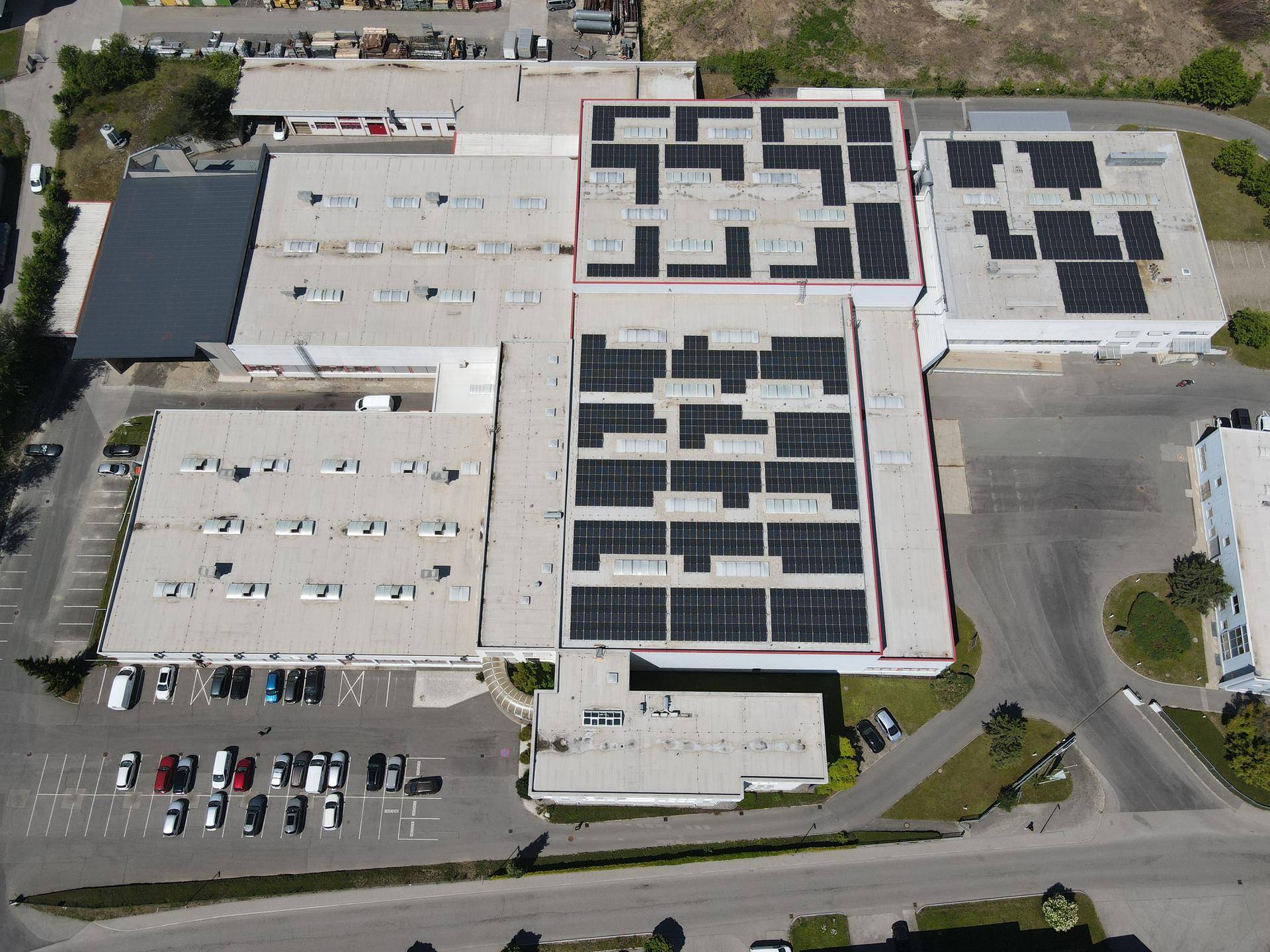 Hochauflösende Luftaufnahme des gesamten Industriekomplexes mit zahlreichen Gebäuden und ausgedehnten Solaranlagen.