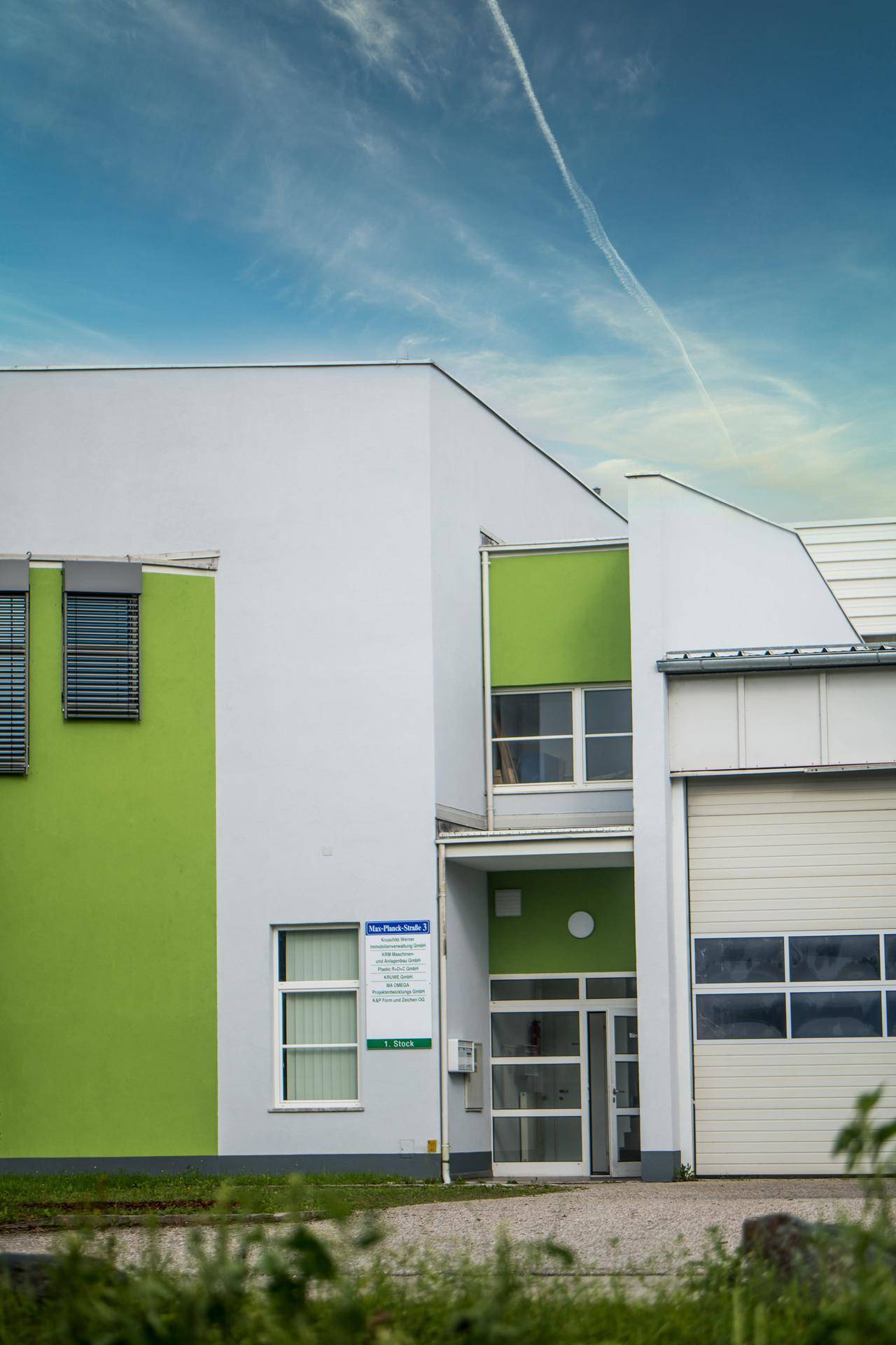 Nahaufnahme des modernen Gebäudeeingangs mit weißer und grüner Fassade unter blauem Himmel.