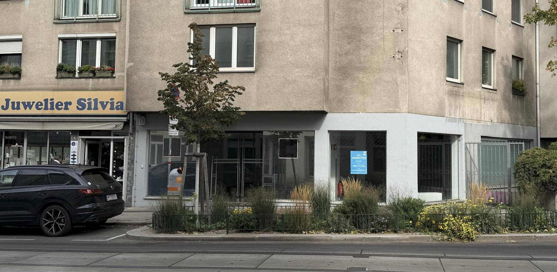 Vorderansicht der Geschäftsräume im Erdgeschoss von der gegenüberliegenden Straßenseite mit mehreren Ladenfronten.