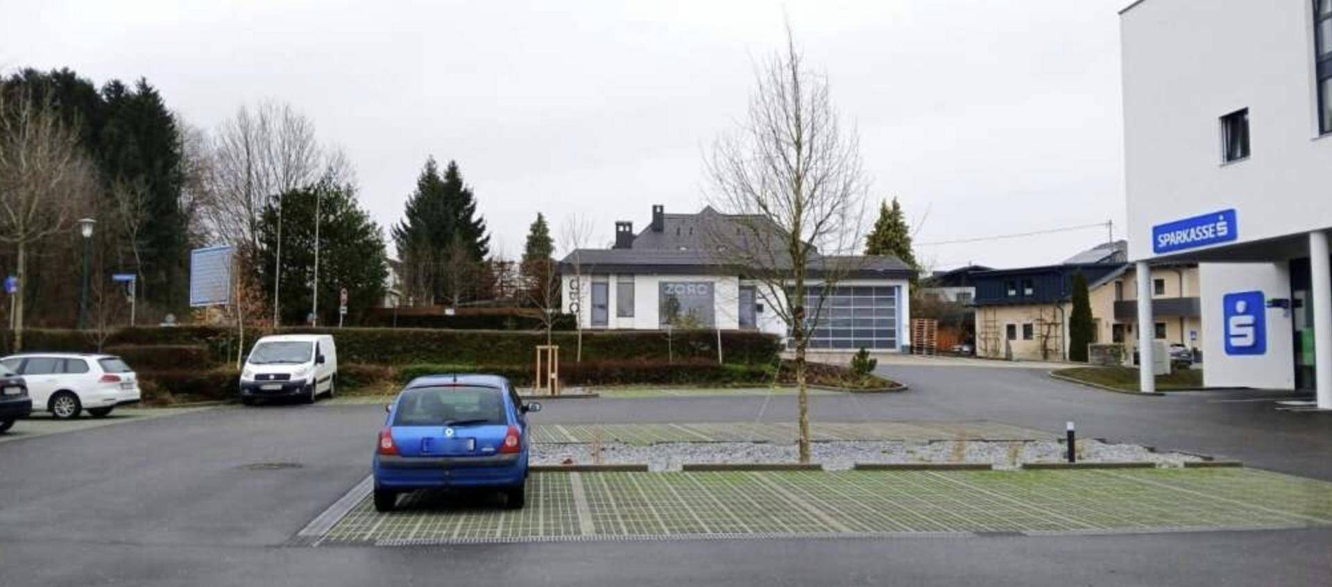 Außenansicht des Parkplatzes mit dem Sparkassen-Gebäude im Hintergrund und weiteren Gebäuden.