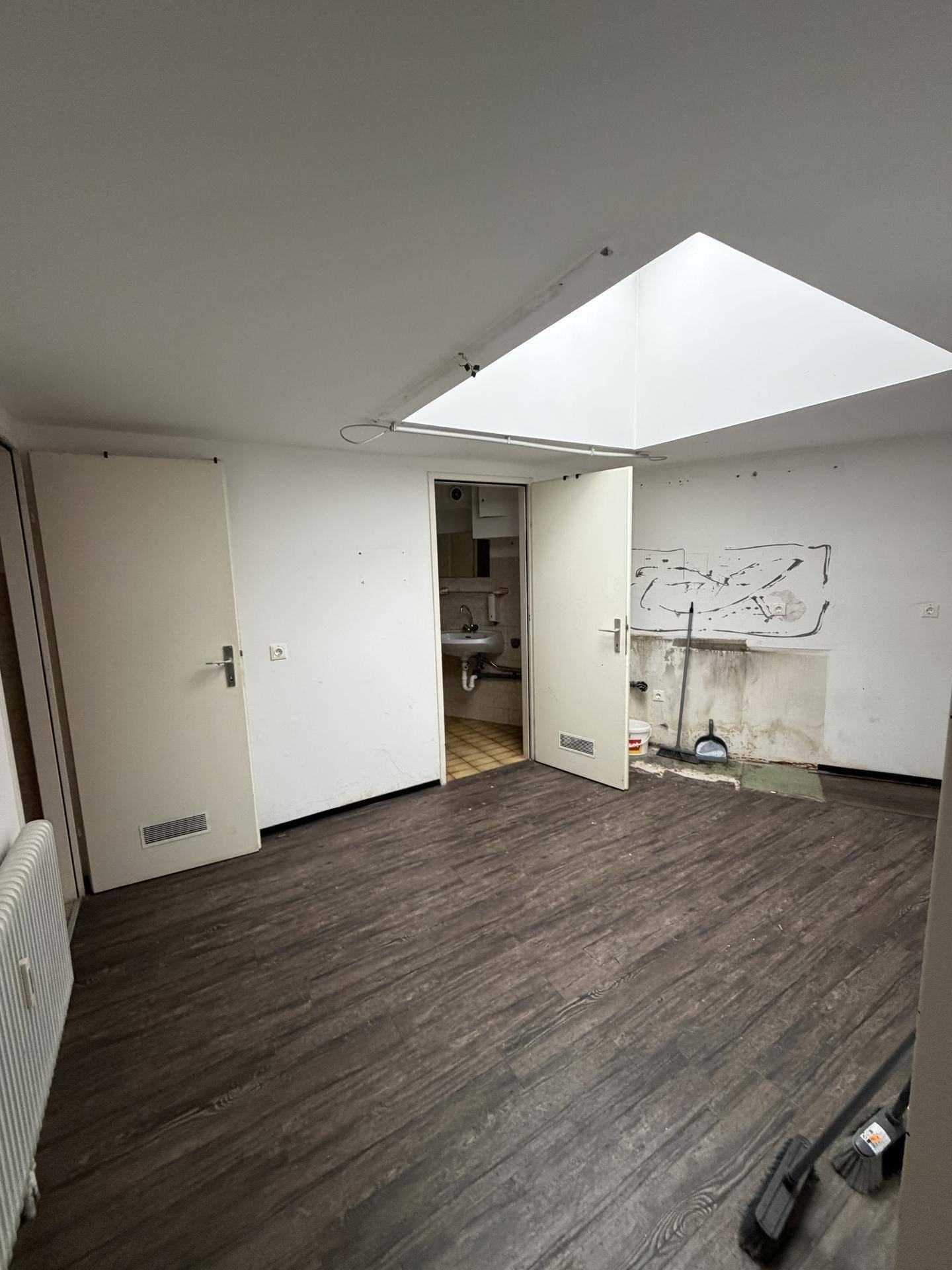 Innenraum mit Dachfenster, dunklem Boden und zwei Türen, die zu einem kleinen Nebenraum führen.