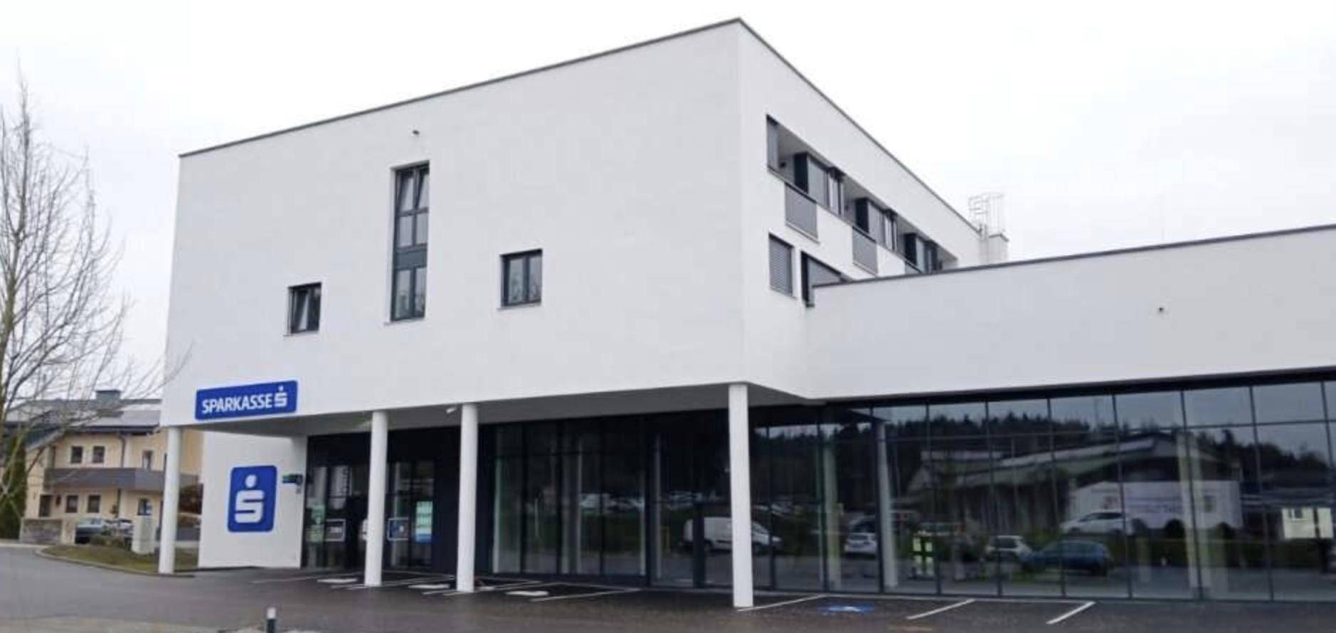 Ansicht des modernen weißen Gebäudes mit Sparkassen-Eingang und großen Glasfronten im Erdgeschoss.