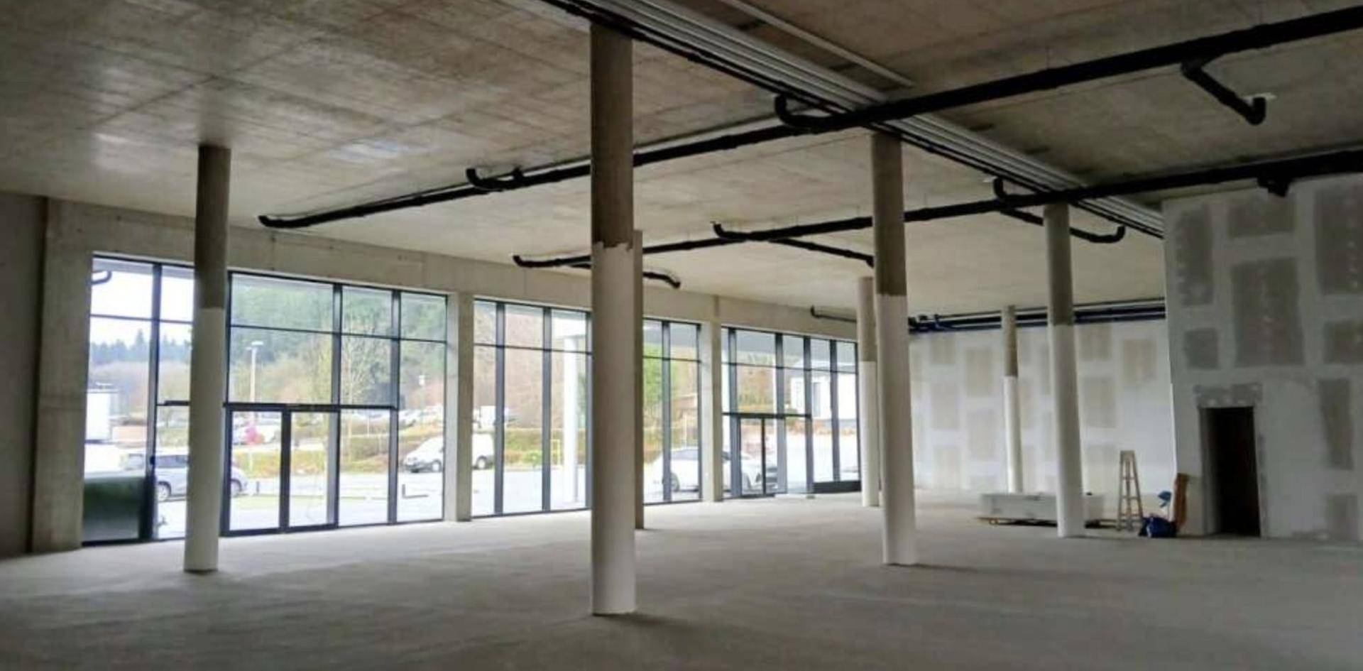 Großer, unfertiger Gewerberaum mit Betondecken, Säulen und hohen Fenstern zur Außenseite.