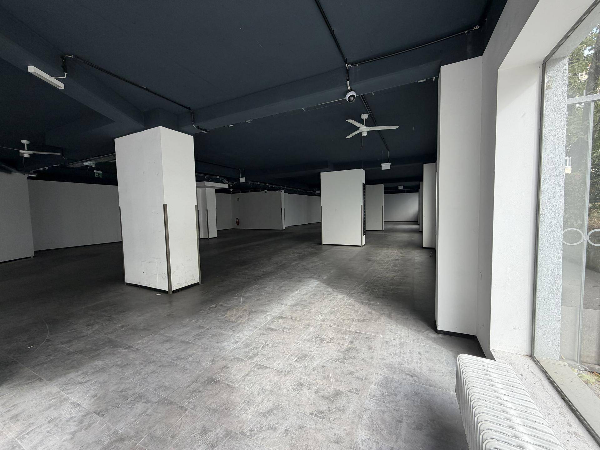 Großer, leerer Geschäftsraum mit dunkler Decke, weißen Säulen und großen Fenstern für viel Tageslicht.